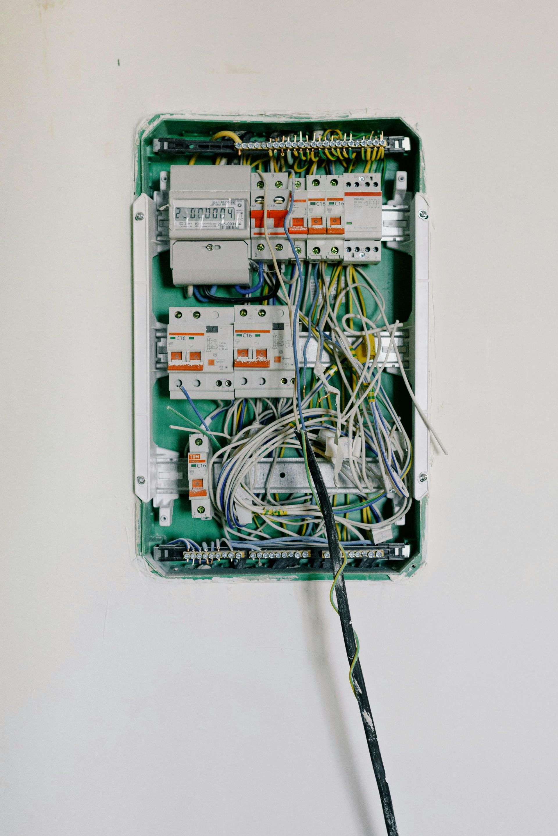 Green electrical panel mounted on a white wall, filled with wires and circuit breakers.