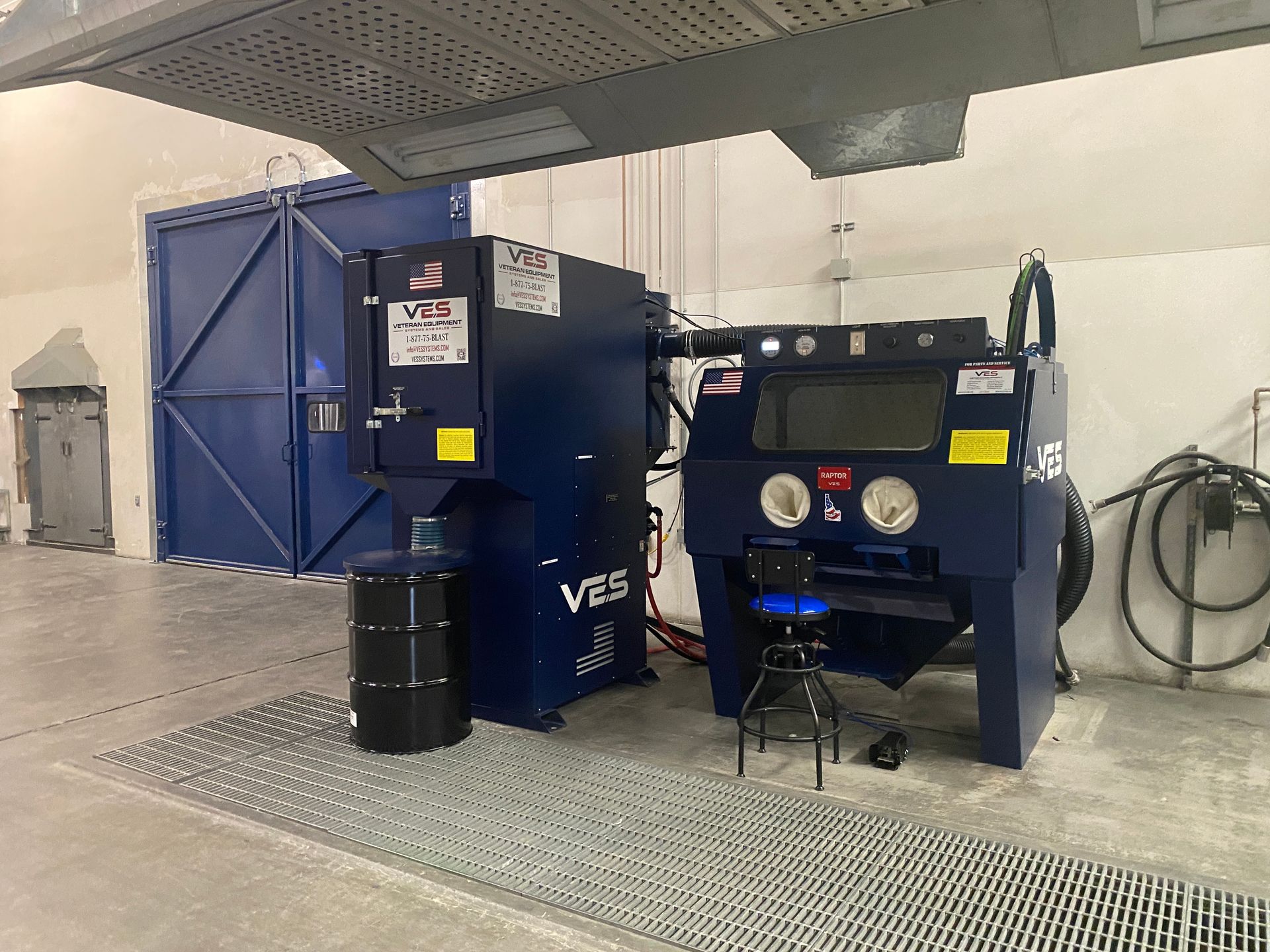 Blue industrial sandblasting equipment in a large room. Includes cabinet, dust collector, and barrel.