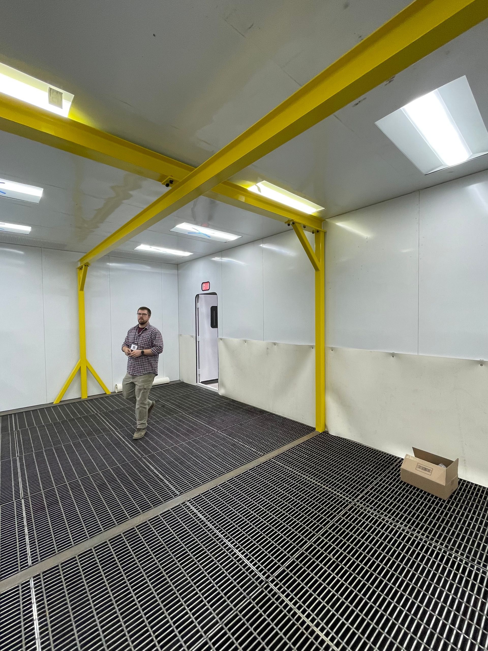Man standing inside white VES blast enclosure with yellow ceiling and wall mounted beams crisscrossing.