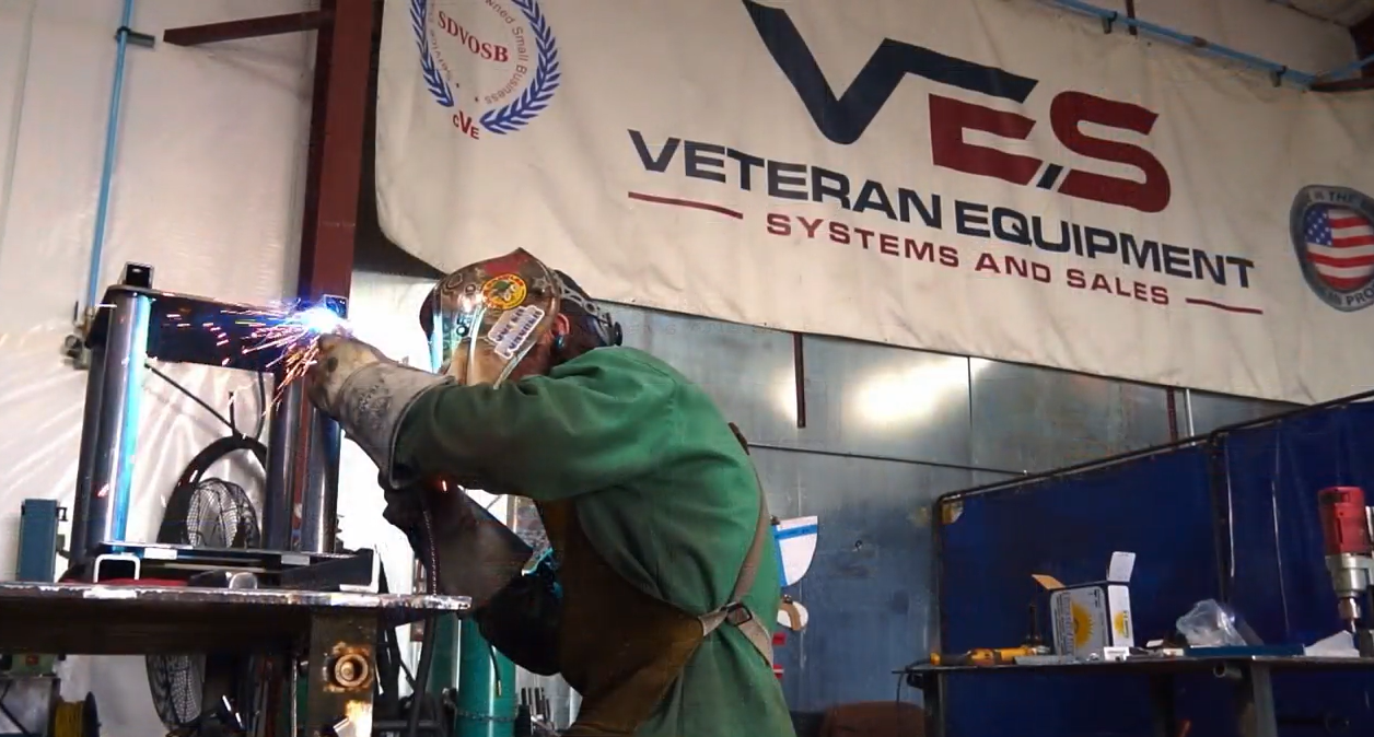 VES technician welding in the shop beneath a Veteran Equipment Systems and Sales banner.