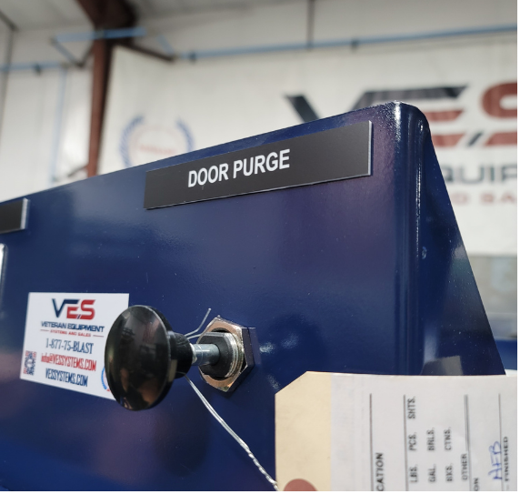Close-up of VES Viper Series blast cabinet door purge control and safety labeling on blue cabinet housing