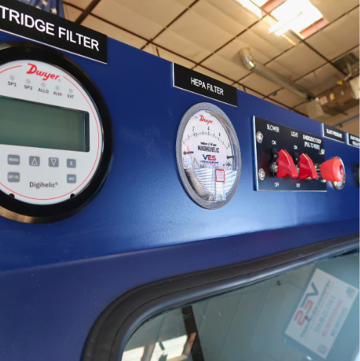 Close up of blast cabinet control panel with cartridge filter gauge, HEPA filter gauge, emergency stop, and lighting controls