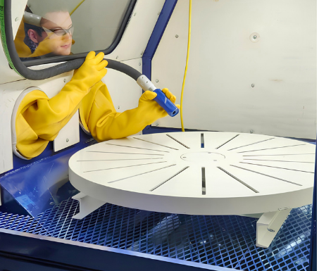 Operator using VES blast cabinet gloves and air blowdown tool inside the cabinet workspace with rotating worktable