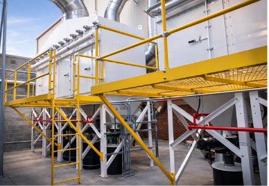 Multiple large white VES dust collectors with yellow railing and platforms installed outside a facility.