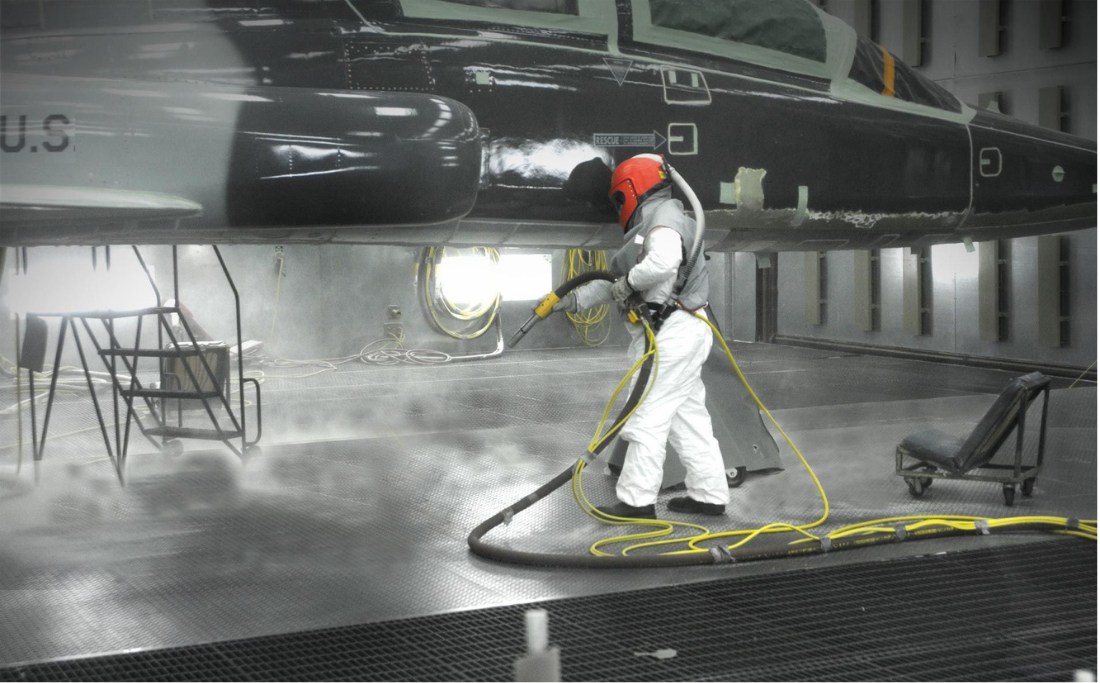 Worker performing aircraft surface preparation inside a corrosion control facility