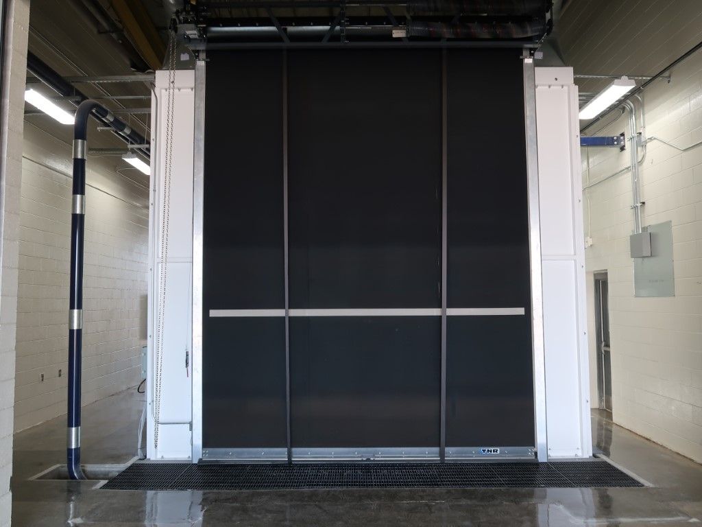 Black roll-up blast booth door outside a VES blast enclosure