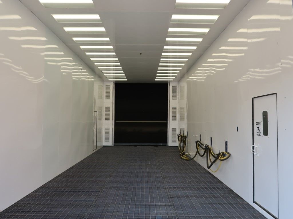 Interior of white VES blast booth with LED lighting and hoses hanging on the wall.