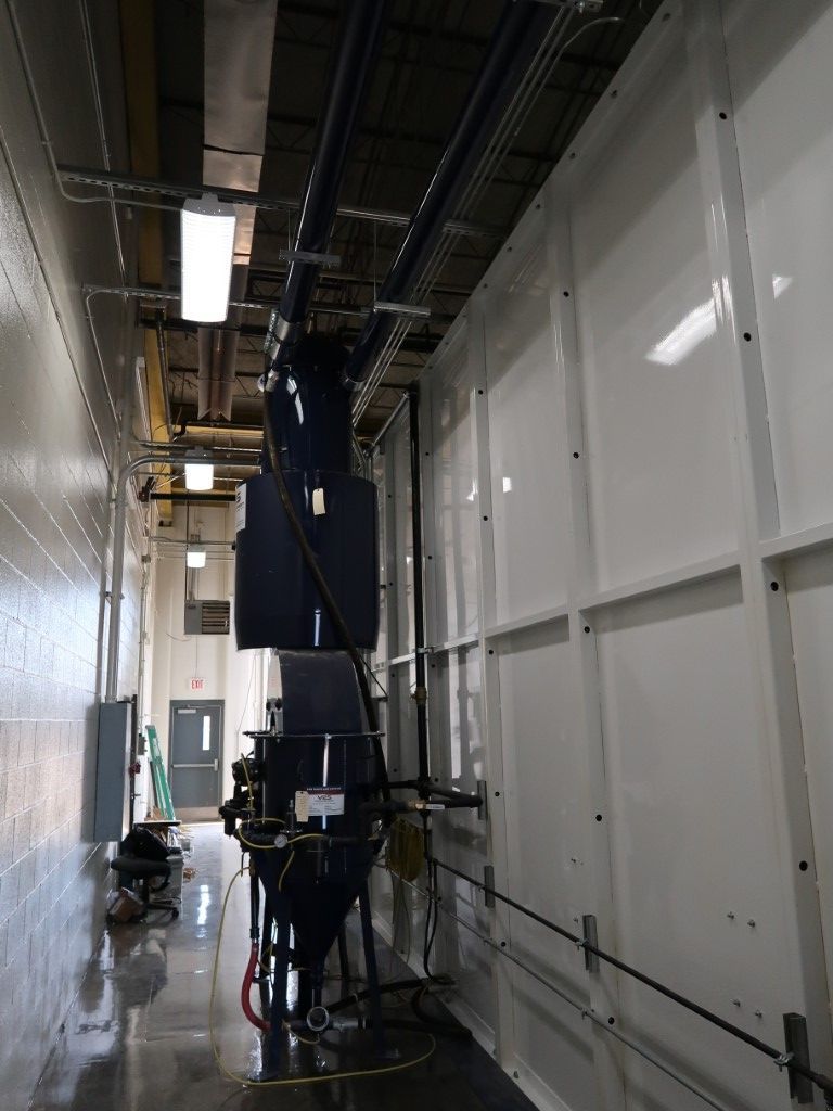 Exterior of large white VES blast enclosure with a blue VES dust collector next to it installed inside a facility.