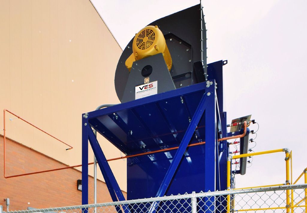 Blue VES dust collector installed outside a building with yellow railing inside open chain link fence