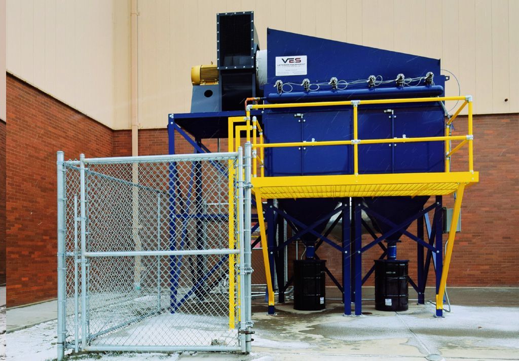 Blue VES dust collector installed outside a building with yellow railing inside open chain link fence
