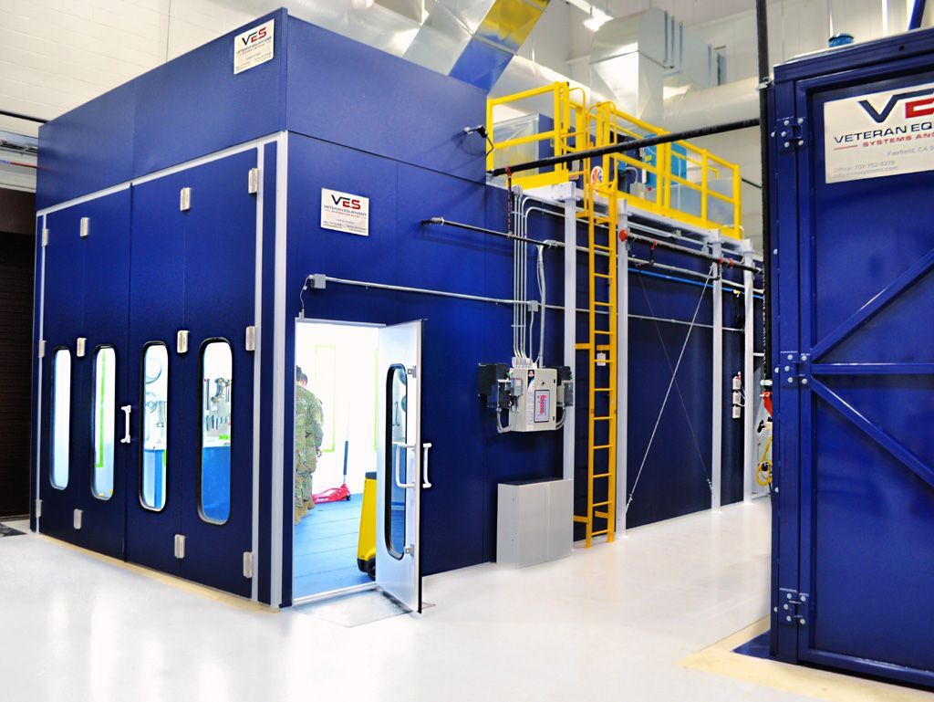 Blue industrial paint booth with doors open, ladder, and exterior equipment.