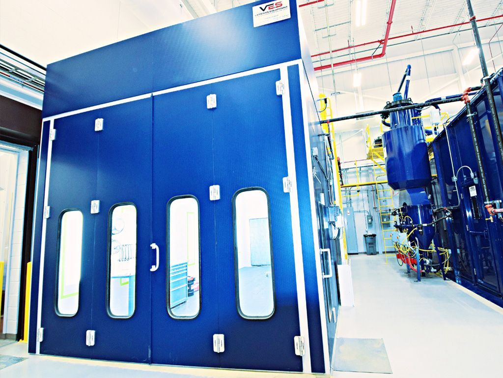 Blue industrial paint booth with windows, in a brightly lit factory setting.