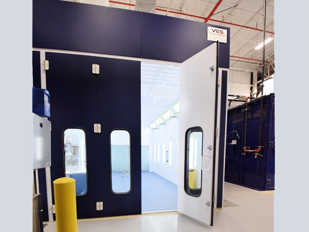 Blue and white paint booth with open door; yellow safety pole.