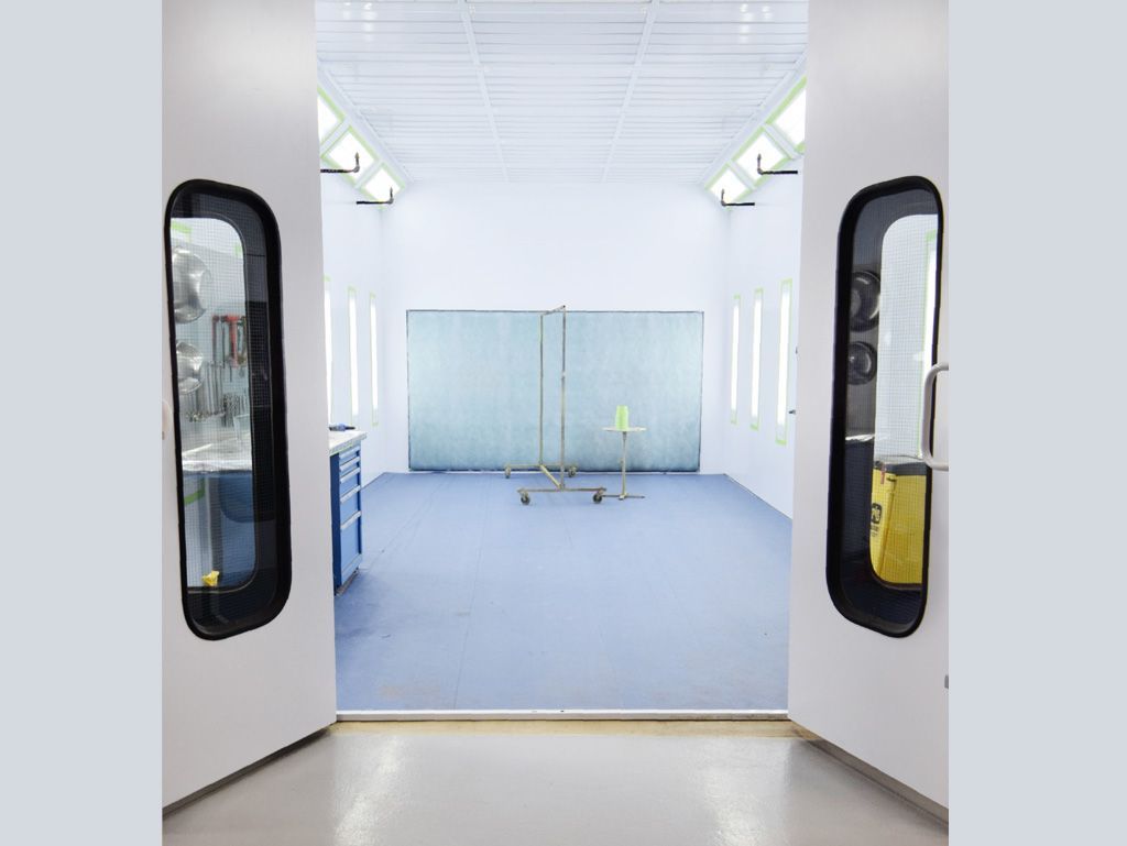 A spray booth with open doors, blue floor, white walls, and metal barriers.