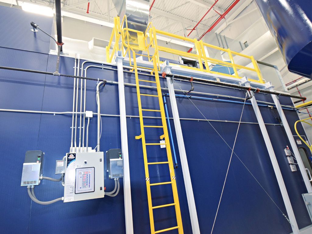 Blue industrial oven with yellow ladder and catwalk. Electrical panels and pipes on the wall.