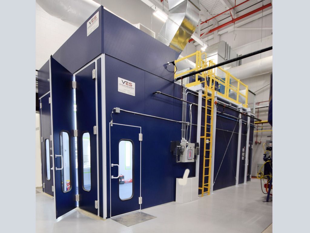 Blue industrial spray booth with doors open in a factory.
