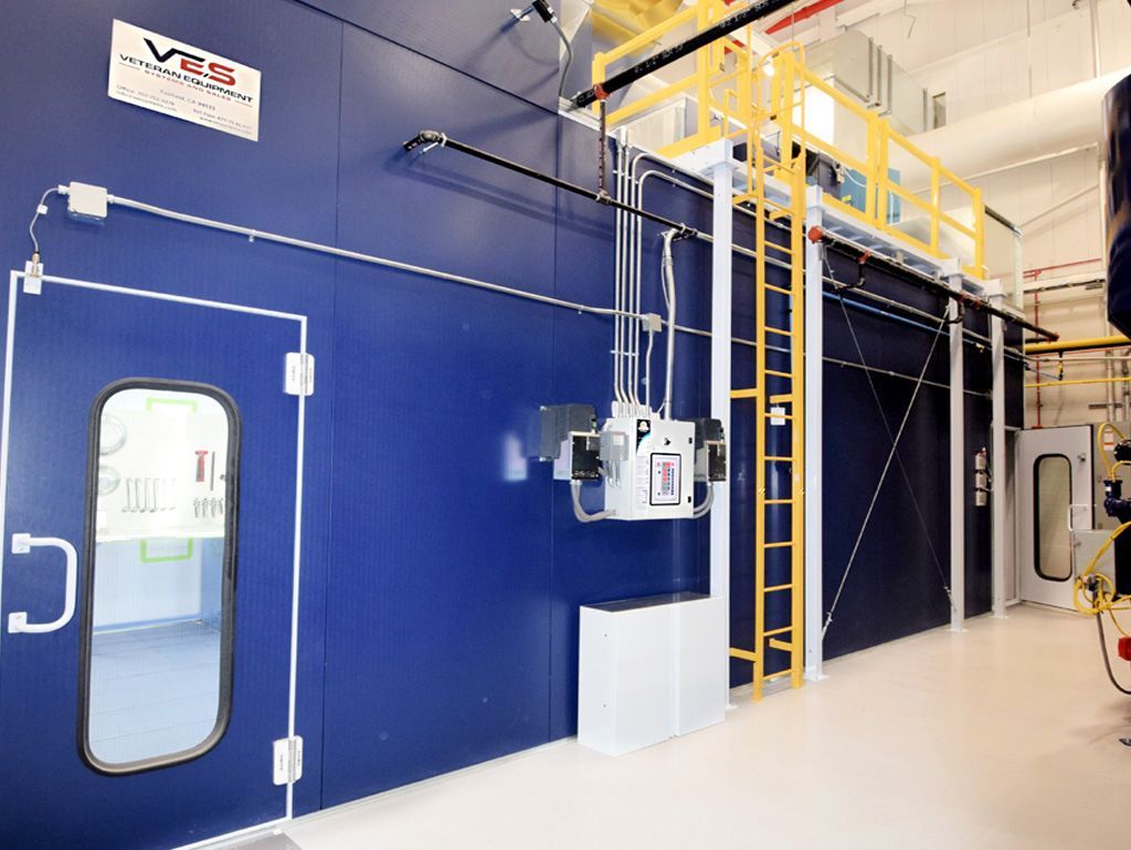 Blue industrial room with door, white box, and hanging machinery. Yellow ladder and platform.
