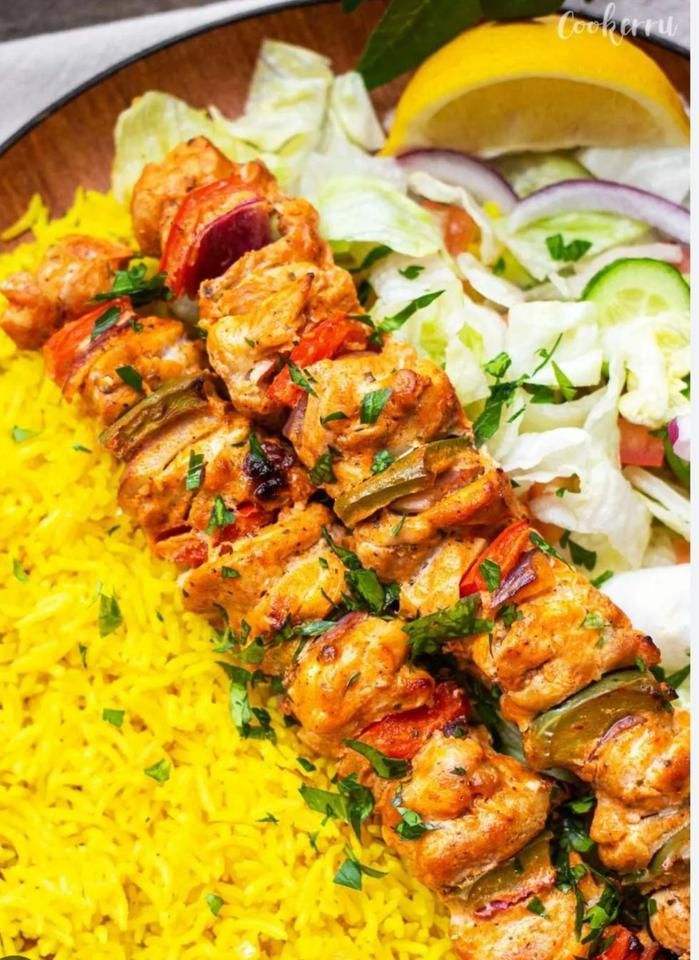 Chicken skewers on yellow rice, served with salad and lemon wedge.