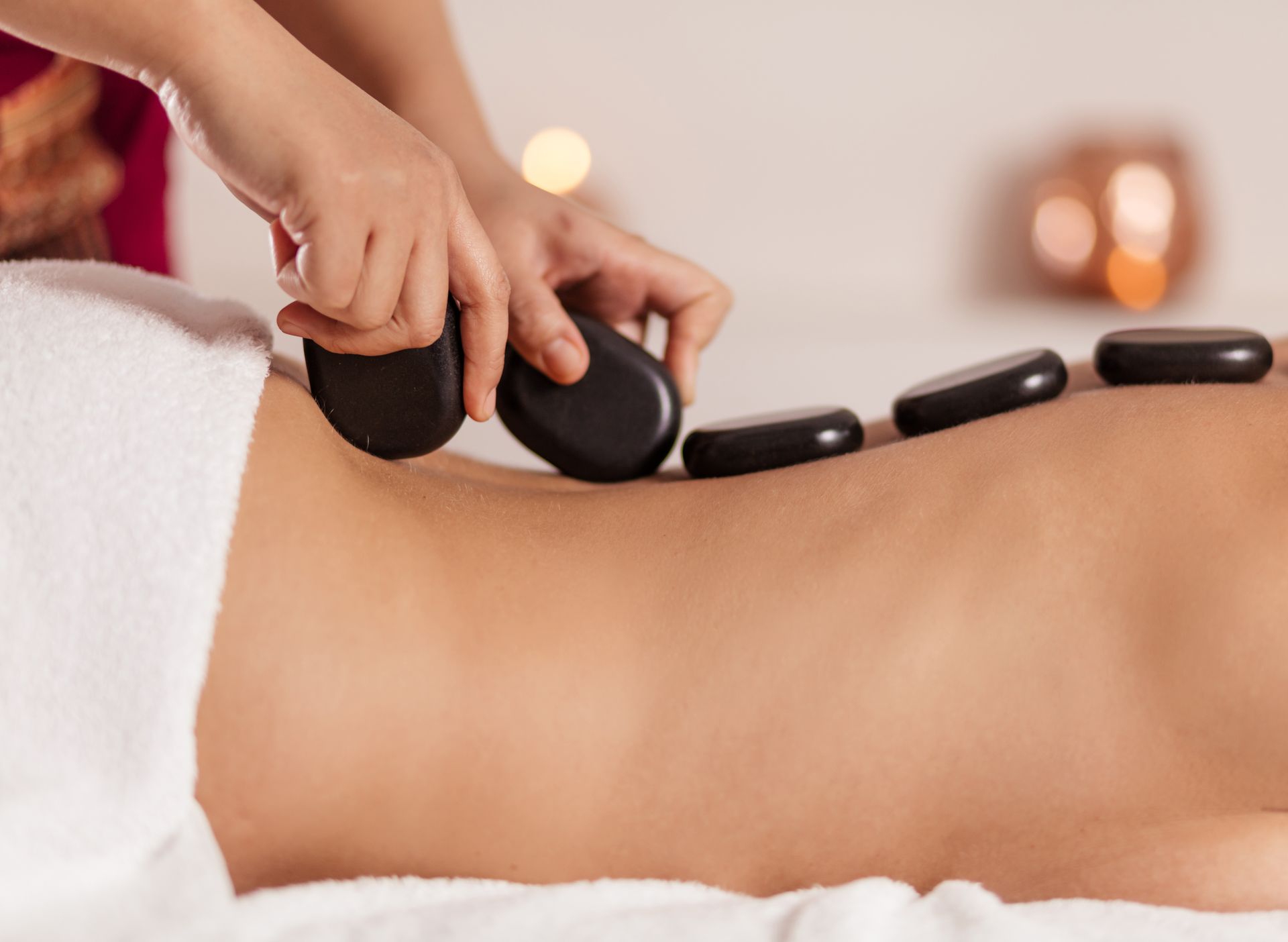 Hot stone massage on a person's back with black stones and a white towel in a spa setting