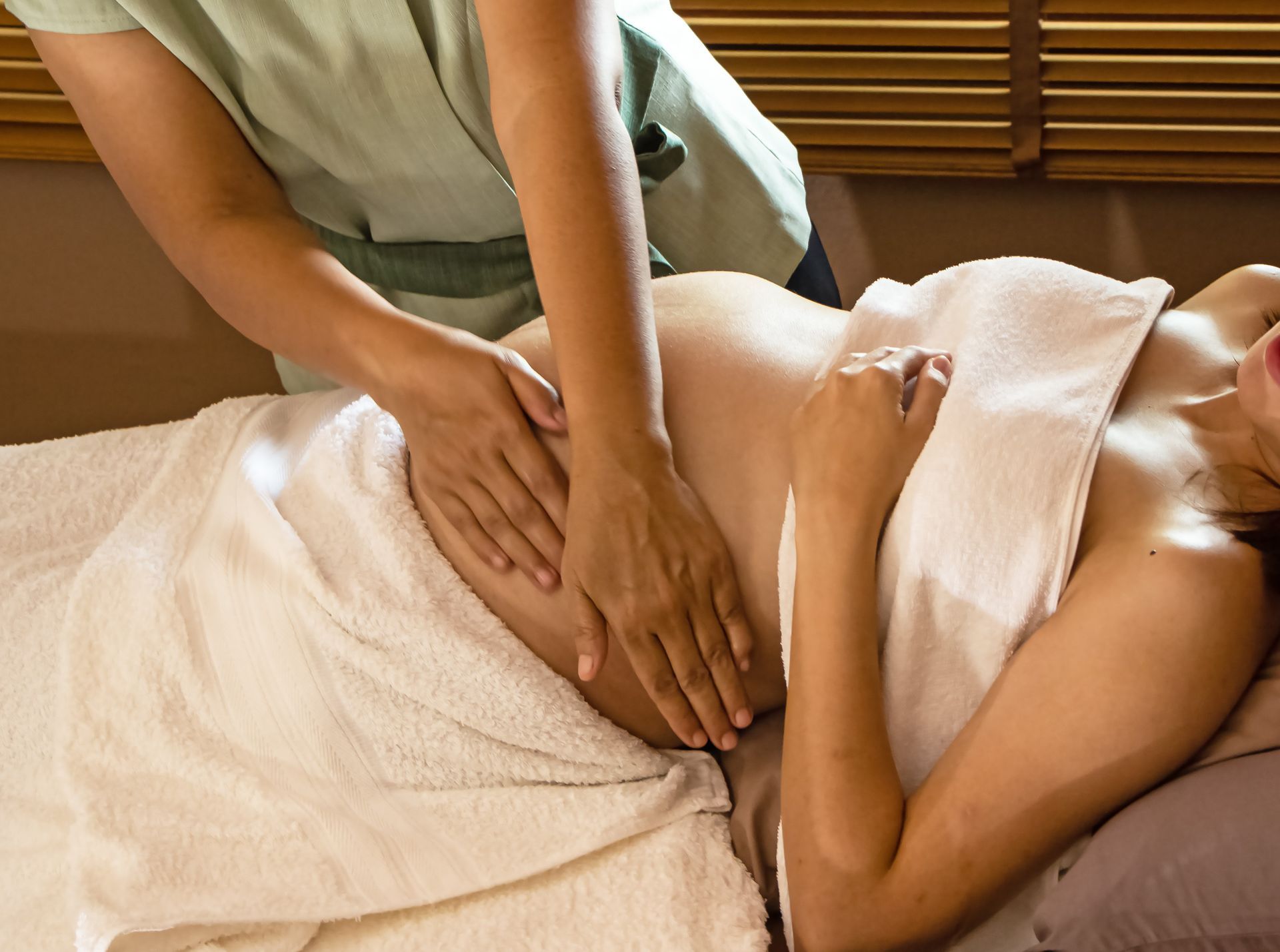 A person receives a back massage on a spa table, covered with a white towel.