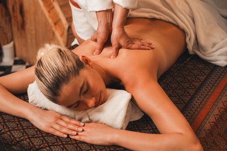 Licensed massage therapist applying firm forearm pressure to a client's upper back during a deep tissue massage session in San Diego