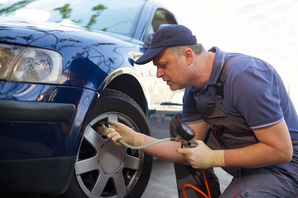 A Man Is Pumping Air Into A Car Tire — Mareeba Motors In Mareeba, QLD