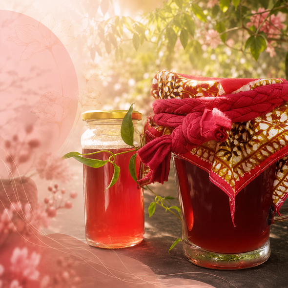 Una bebida festiva roja y un tarro de regalo rojo con cinta sobre una mesa iluminada por el sol, con vegetación y flores al fondo.