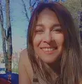 Persona sonriente con cabello castaño largo al aire libre, bajo la cálida luz del sol.