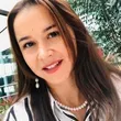 Primer plano de una mujer sonriente con cabello castaño largo y una blusa de rayas, al aire libre entre vegetación.