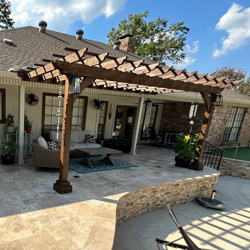 Wooden pergola over a patio with outdoor furniture, and a curved stone wall.