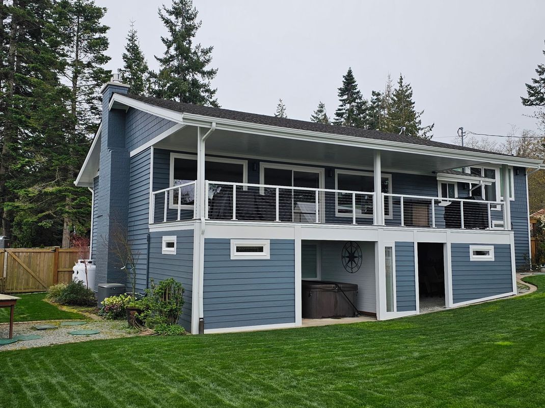 Blue two-story house with white trim, a covered balcony, and a green lawn surrounded by trees.