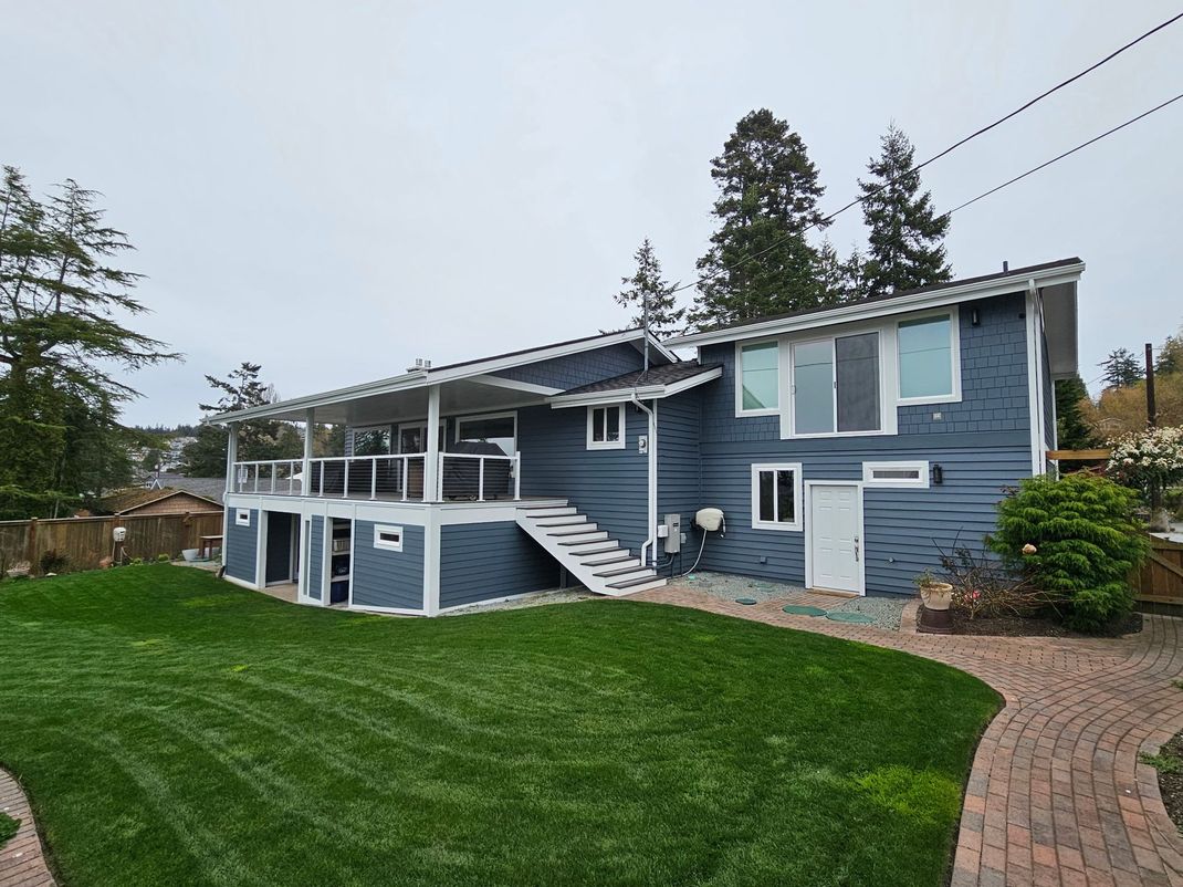 Blue house with white trim, sloped lawn, and brick walkway on an overcast day