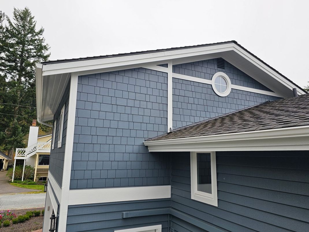 Blue-gray house exterior with a shingled roof, white trim, and a round attic vent