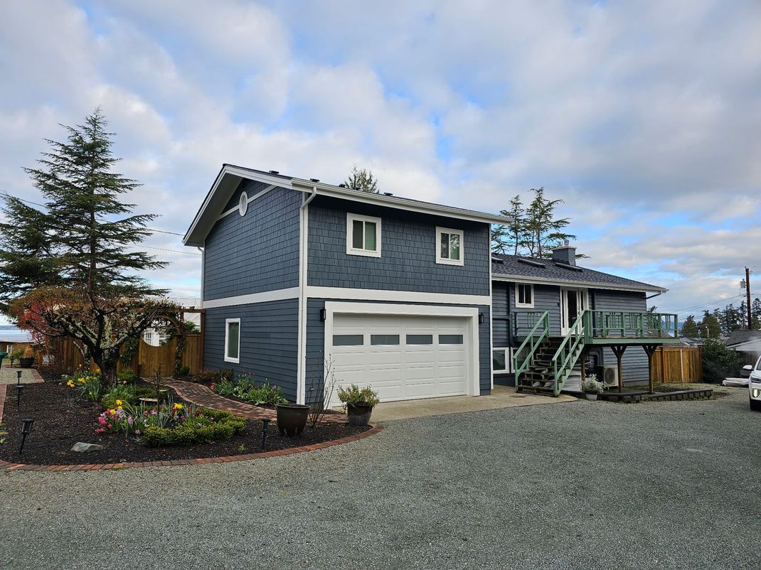 Gray two-story house with white garage on a gravel driveway under a cloudy sky