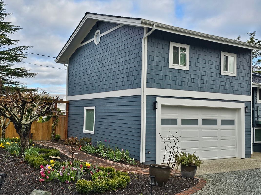 Blue two-story house with white trim, garage, and landscaped front garden under a cloudy sky
