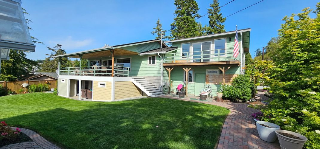 Modern two-story house with green lawn, patio, and trees under a sunny sky