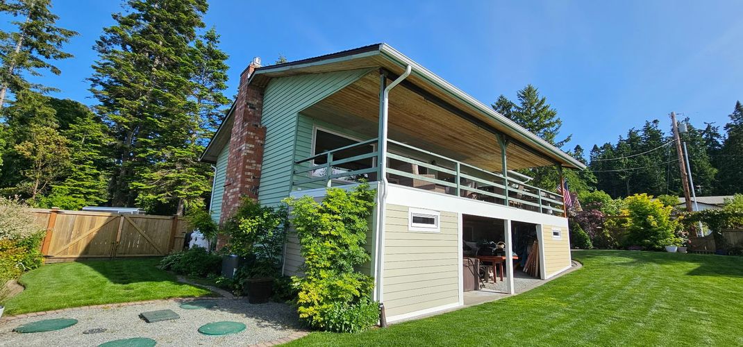 Sunlit backyard with a cream-colored house, covered patio, and green lawn under a blue sky