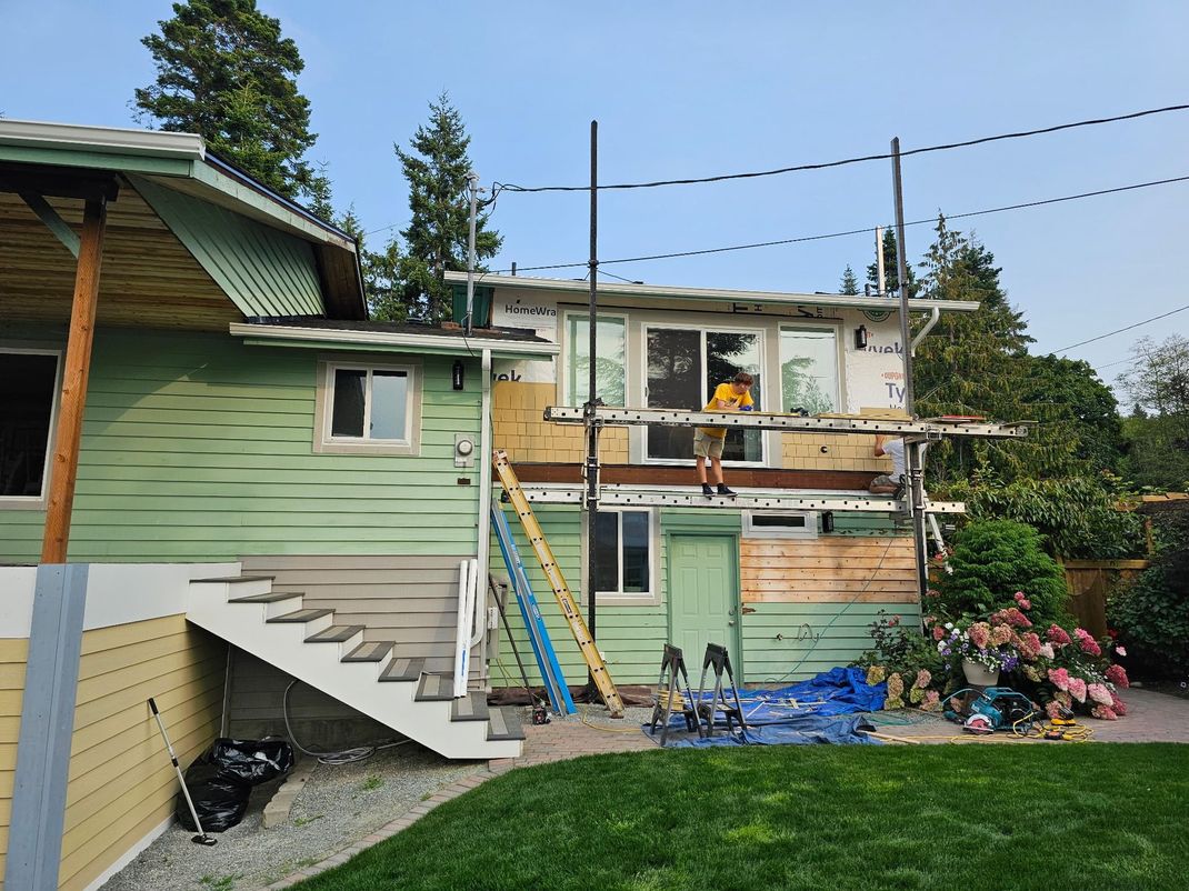 Damaged two-story house with blue tarps, ladders, and scattered debris under repair
