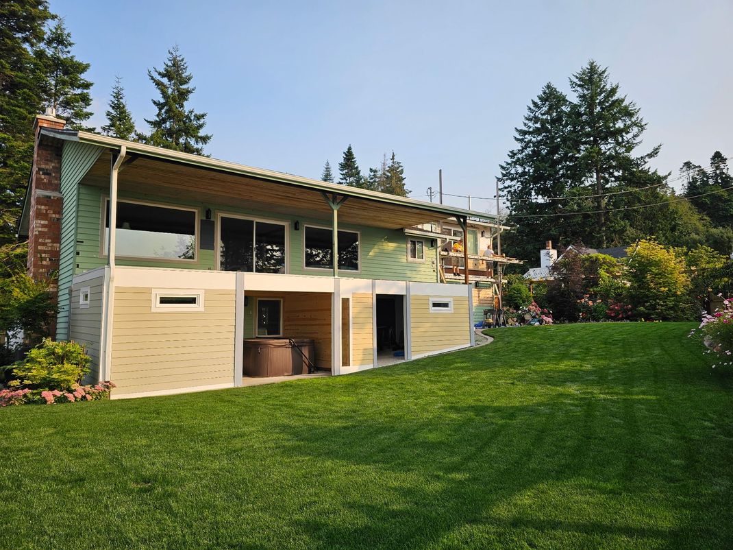 Modern two-story house with a large green lawn and surrounding trees under a clear sky