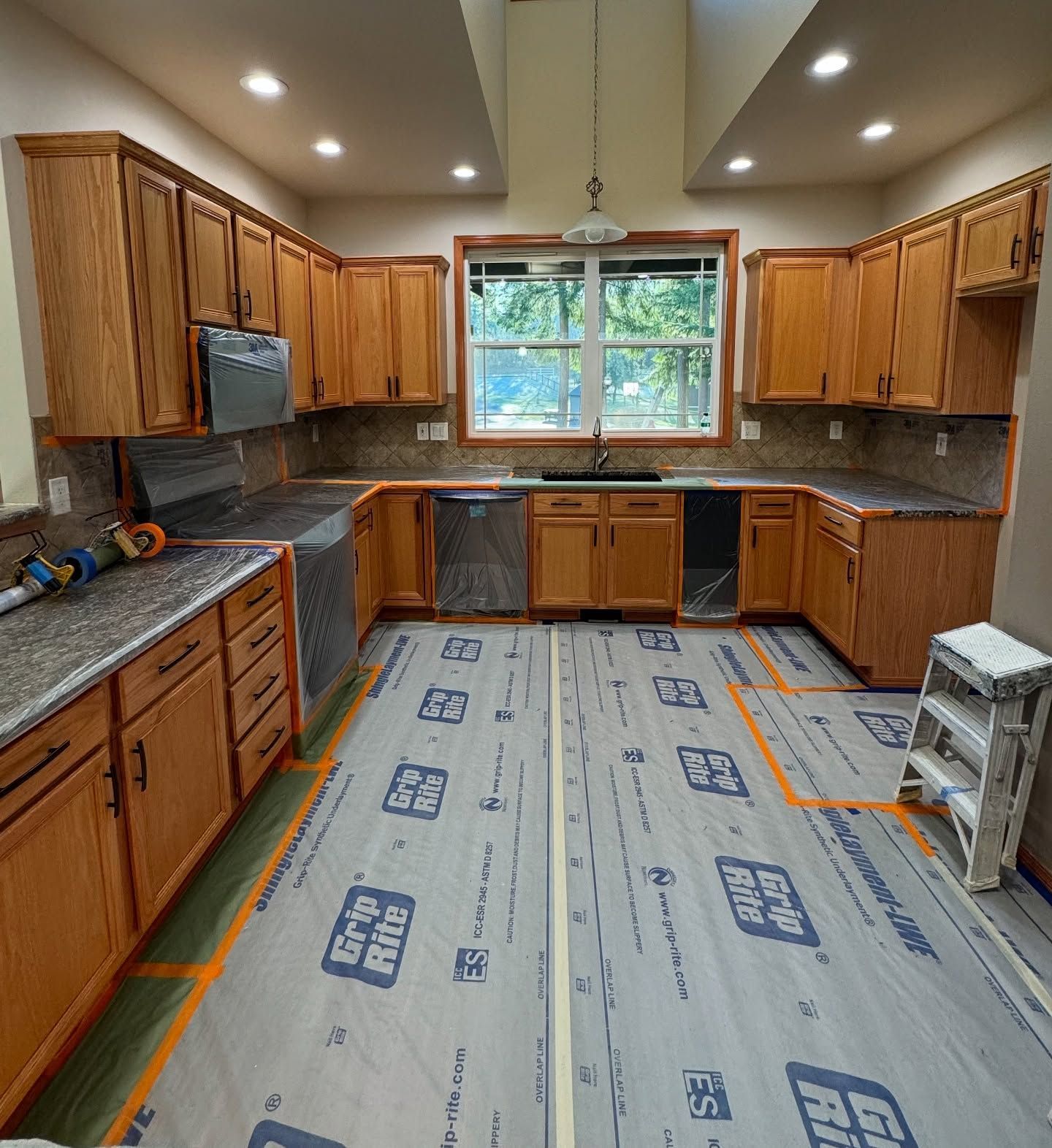 Unfinished kitchen with wood cabinets, granite counters, and a large window over the sink.