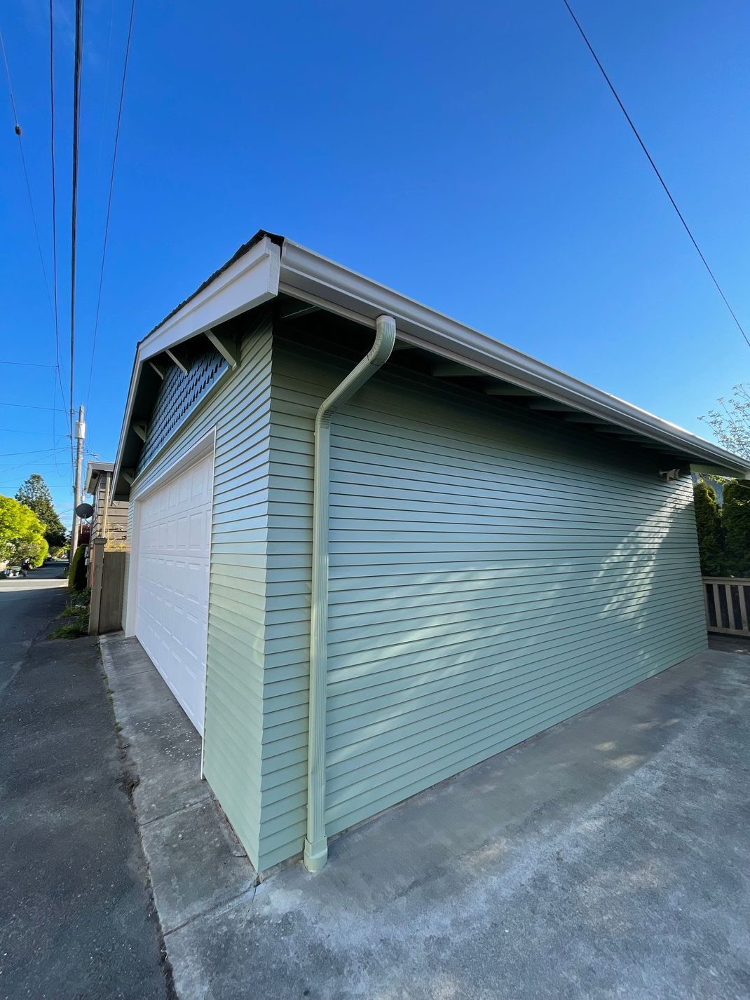 Light gray corrugated metal garage with white trim under a blue sky, viewed from the corner
