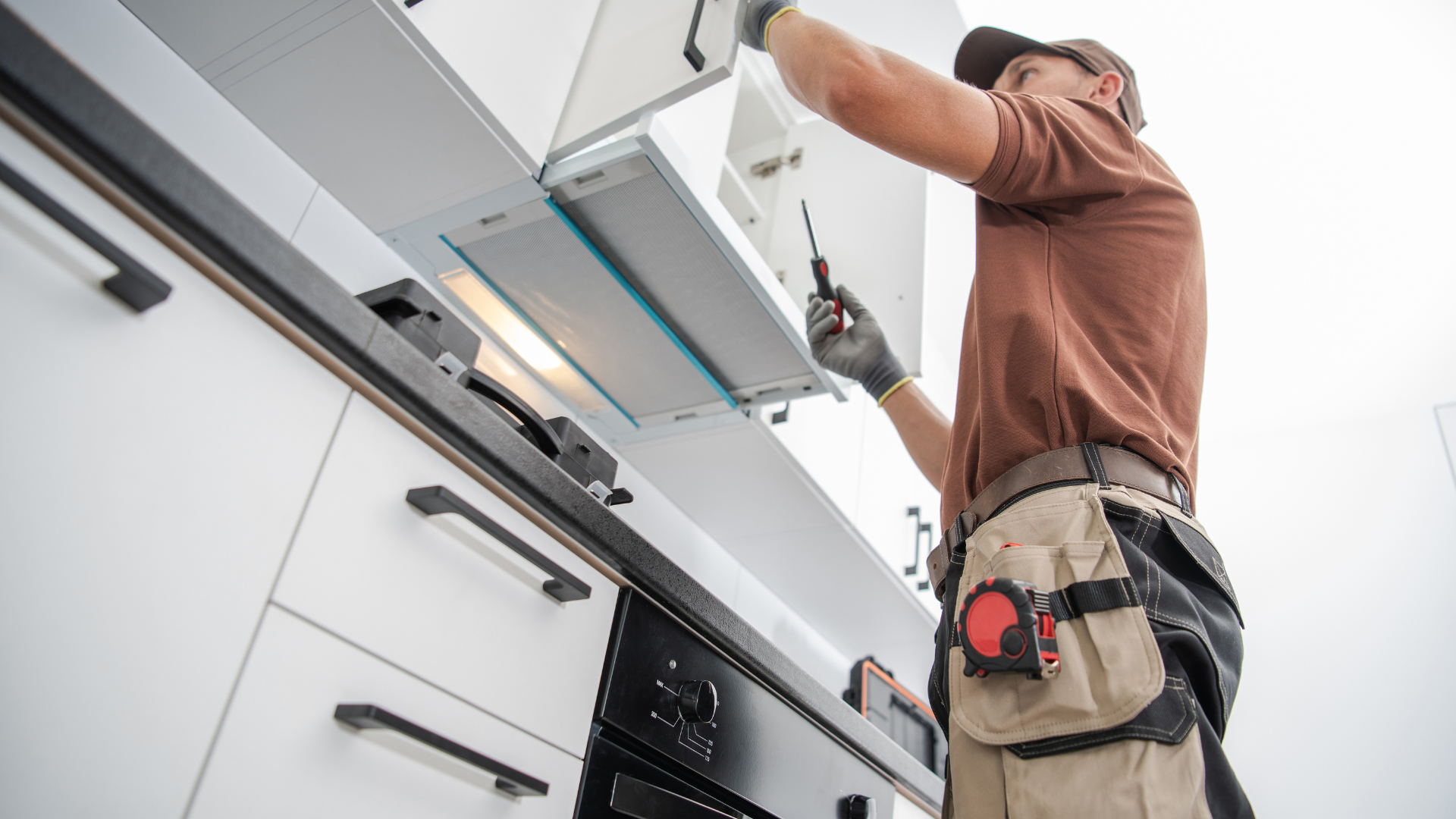 Technician installing a white kitchen cabinet using tools in a bright modern kitchen