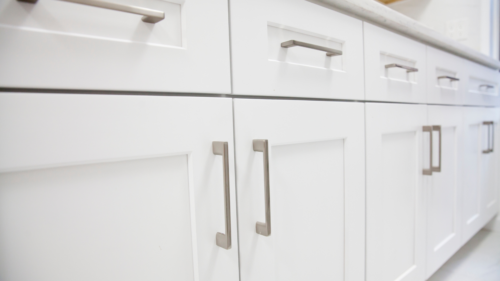 White kitchen cabinets with silver handles and drawers in a bright, modern kitchen.