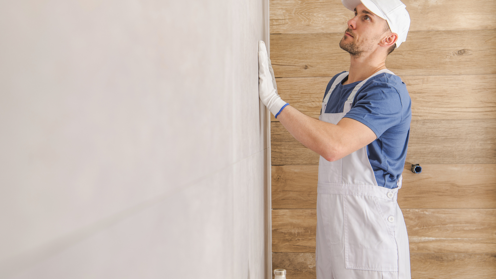 Painter in white overalls and cap applying paint to a wall indoors