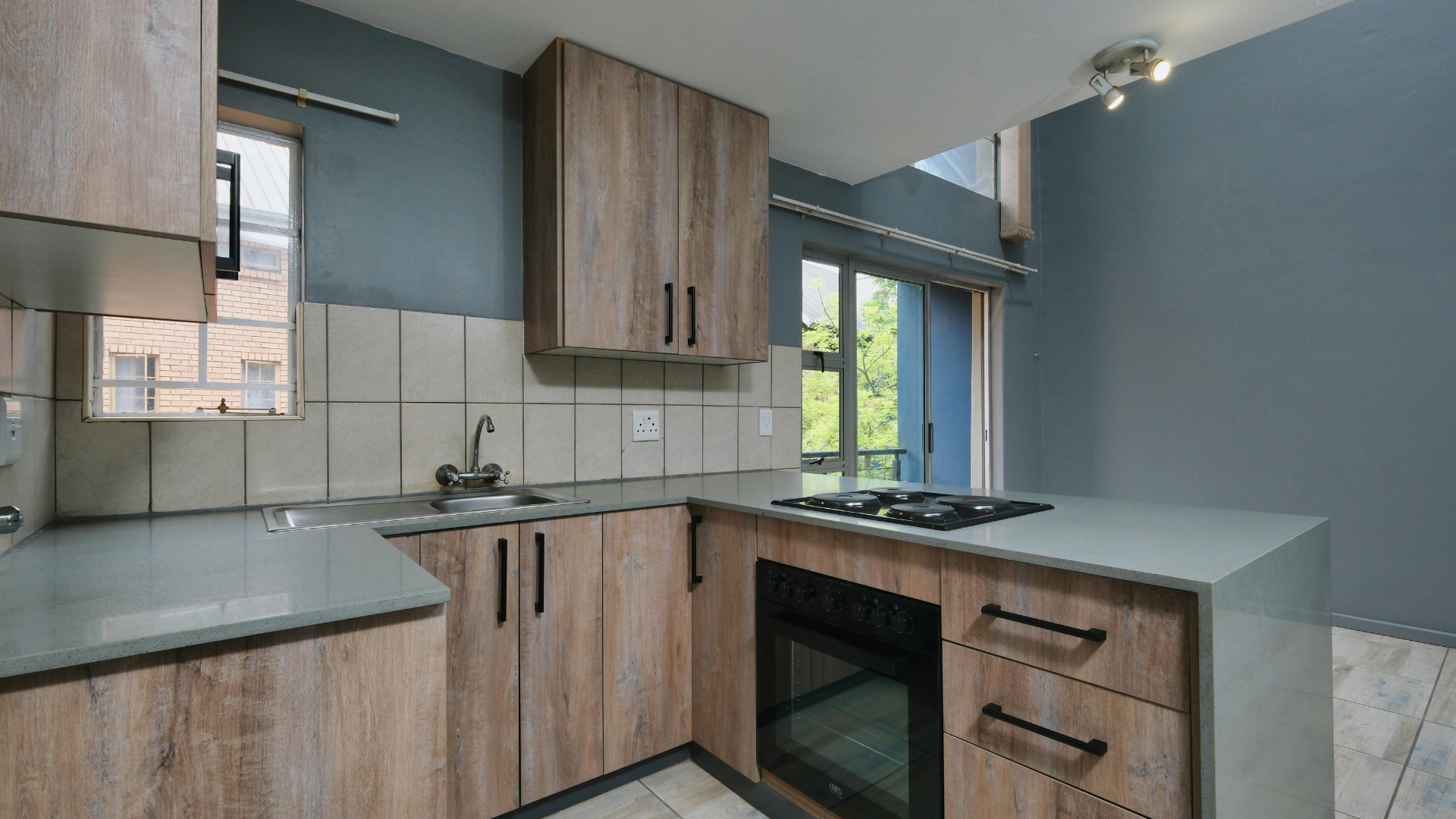 Modern kitchen with wood cabinets, light countertops, stove, sink, and a window overlooking greenery.