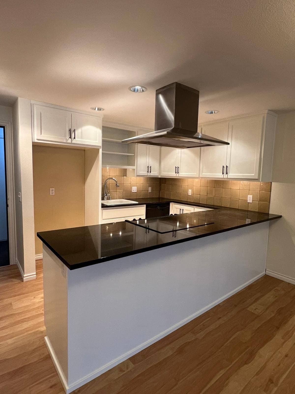 Modern kitchen with white cabinets, black granite island, stainless range hood, and wood floors