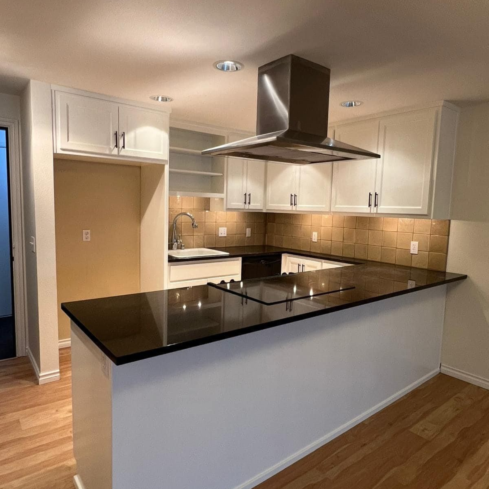 Modern kitchen with white cabinets, black granite island, and stainless steel range hood