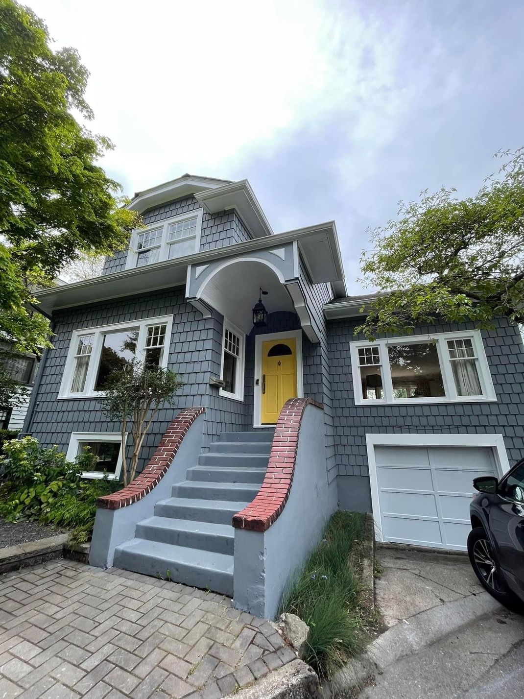 Gray house with pink stair rails, yellow front door, and a white garage under a cloudy sky