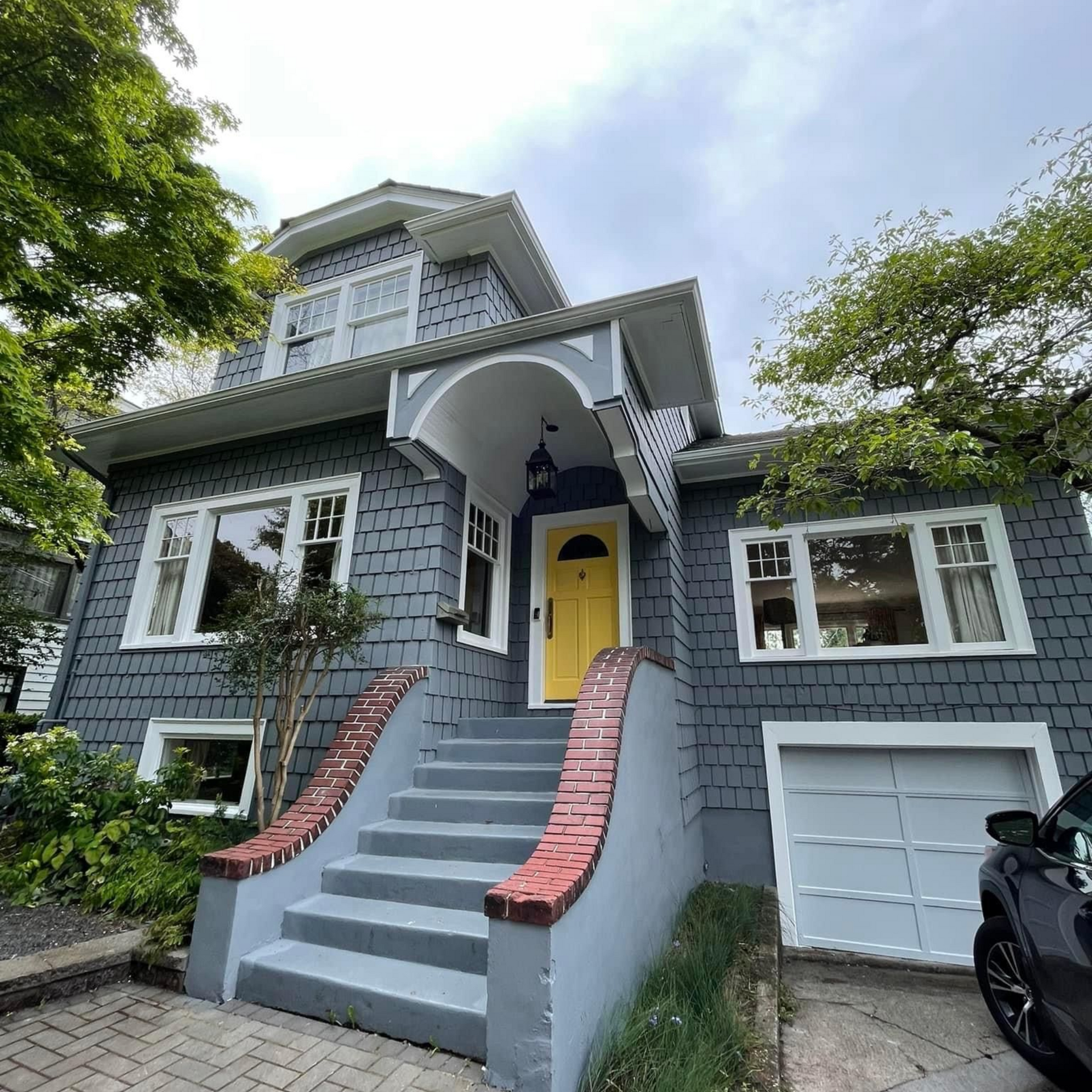 Gray house with yellow front door, white trim, and red-brick stair railings under trees