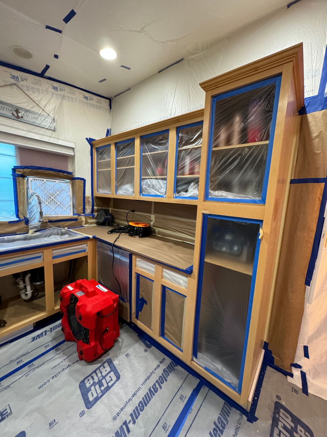 Small workshop kitchen with wooden cabinets, sink, countertop, and a red tool bag on the floor.